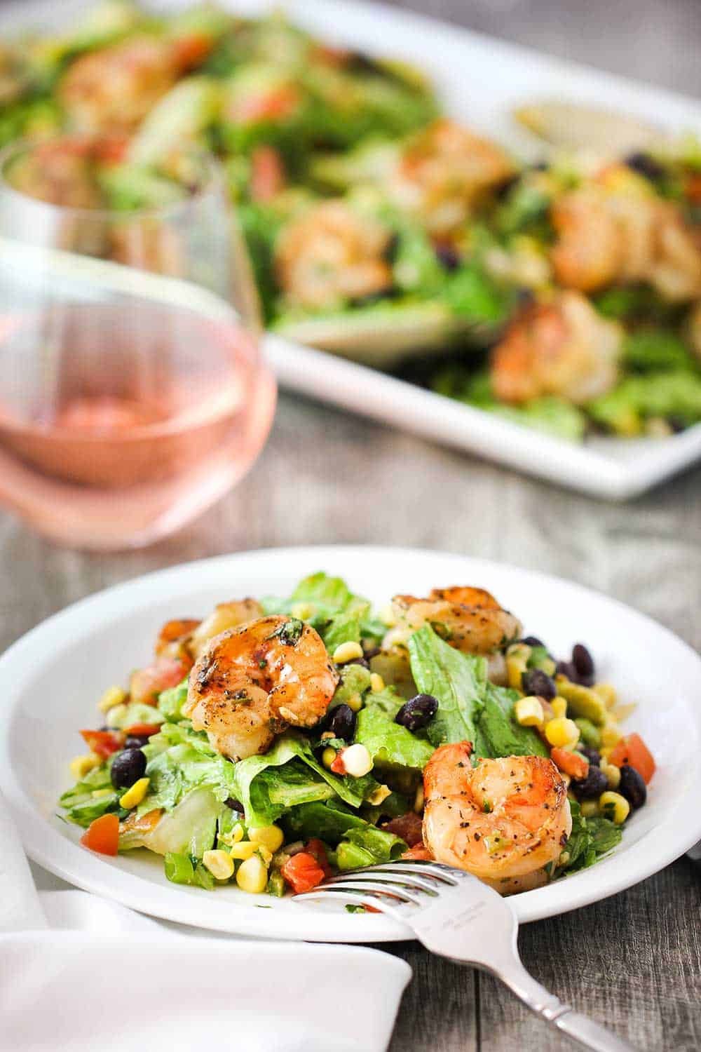 Grilled shrimp, corn & avocado salad on a single serving plate with a glass of wine nearby. 