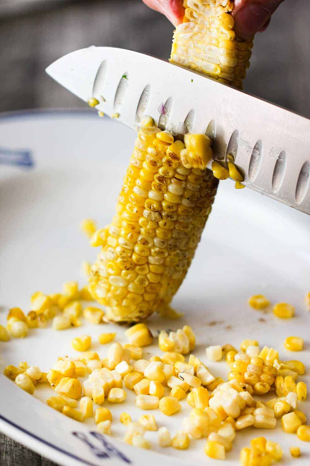 Use a sharp knife to remove the kernels from the cob for the grilled shrimp salad. 