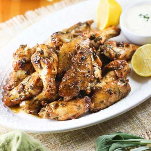 Italian Style Chicken wings on a white plate with lemon and dipping sauce