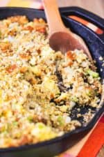 A large cast iron skillet filled with Thanksgiving dressing with a wooden spoon in it.