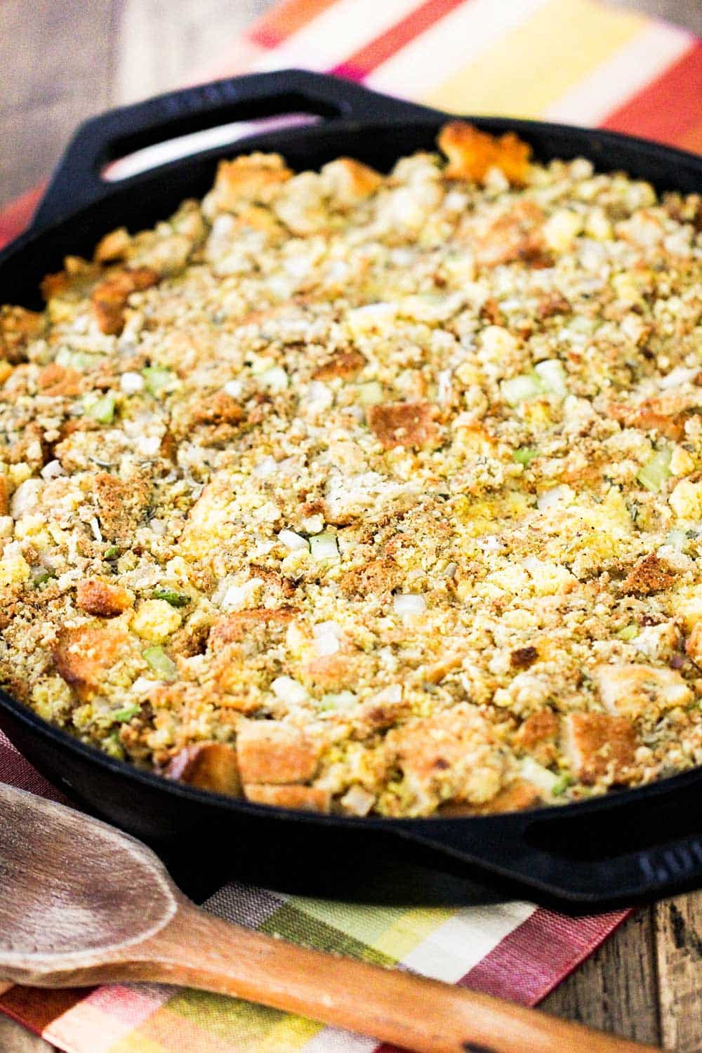 A large cast iron skillet filled with Mom's Thanksgiving dressing next to a wooden spoon. 