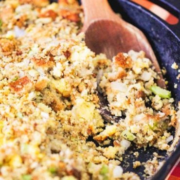 A close up view of a wooden spoon in a pan of Thanksgiving dressing.