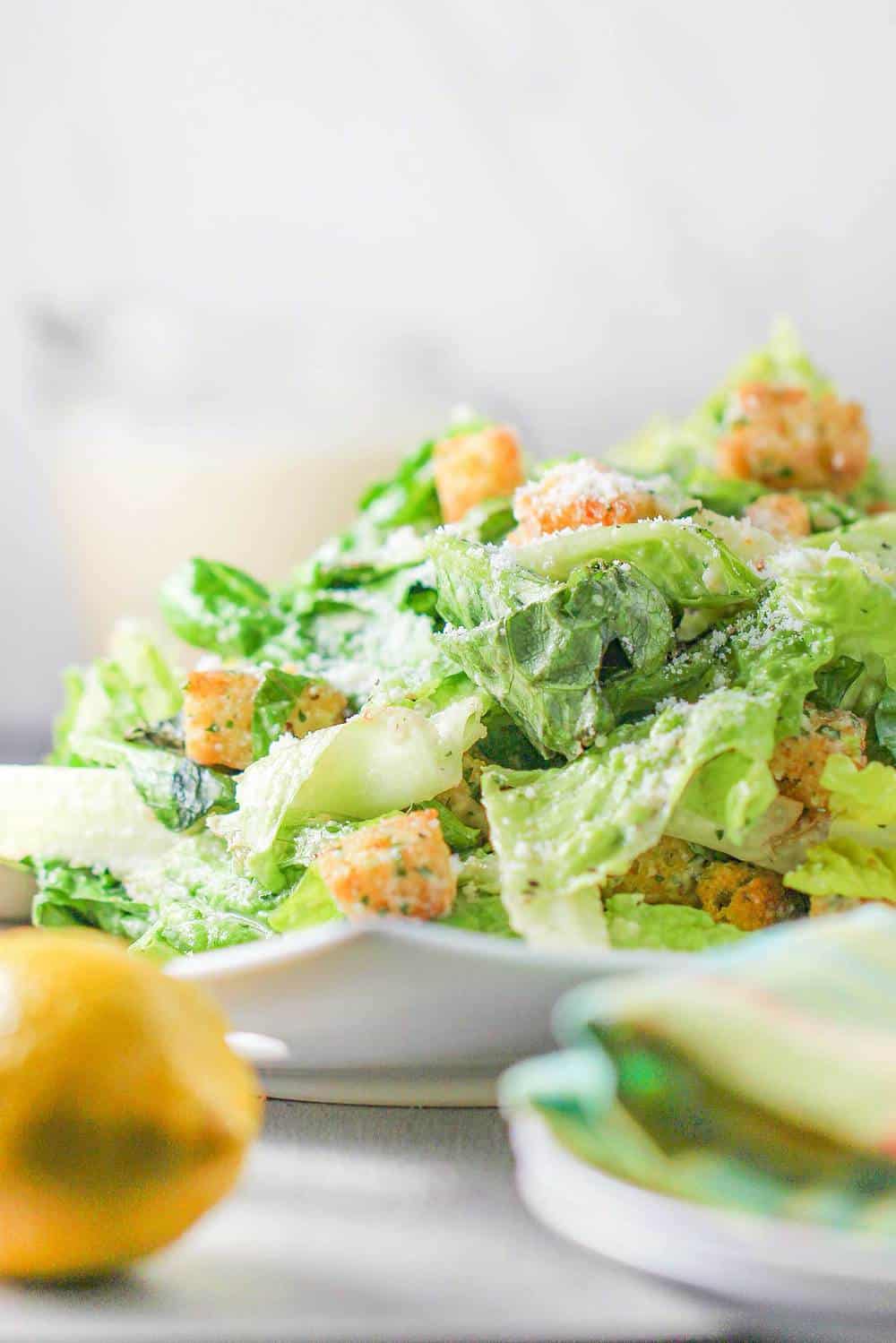 A white plate holding a classic Caesar salad with a lemon nearby. 