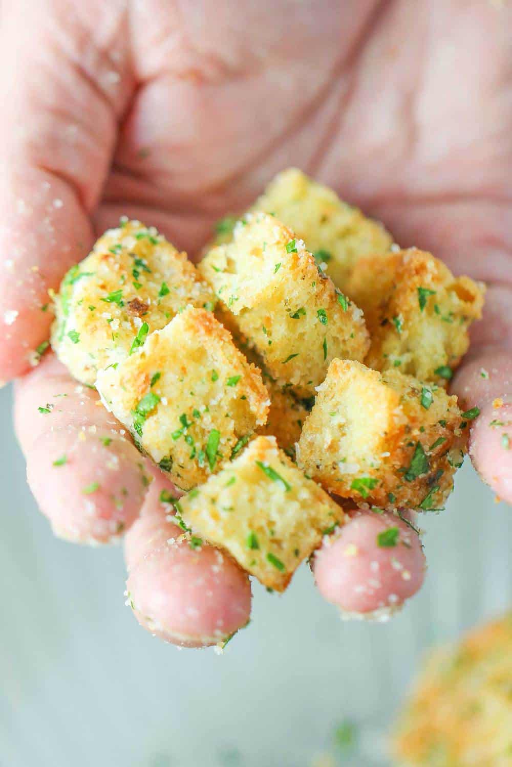 A hand holding homemade croutons for classic Caesar salad. 