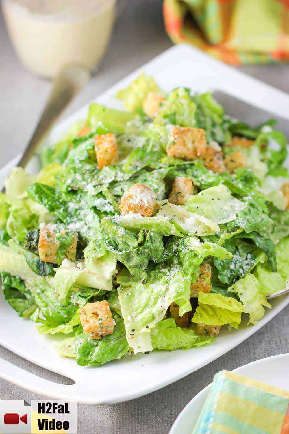 A large Caesar salad on a white plate with a colorful napkin nearby. 