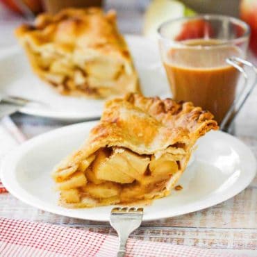 A close-up view of a slice of homemade apple pie next to a glass cup of coffee.