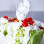 A spoon drizzling homemade blue cheese dressing over a wedge salad.