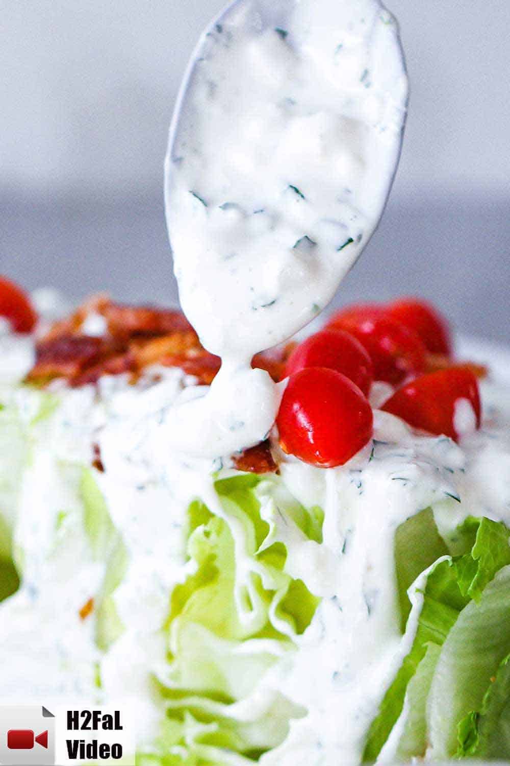 A spoon pouring homemade blue cheese dressing over lettuce with tomatoes and bacon bits. 