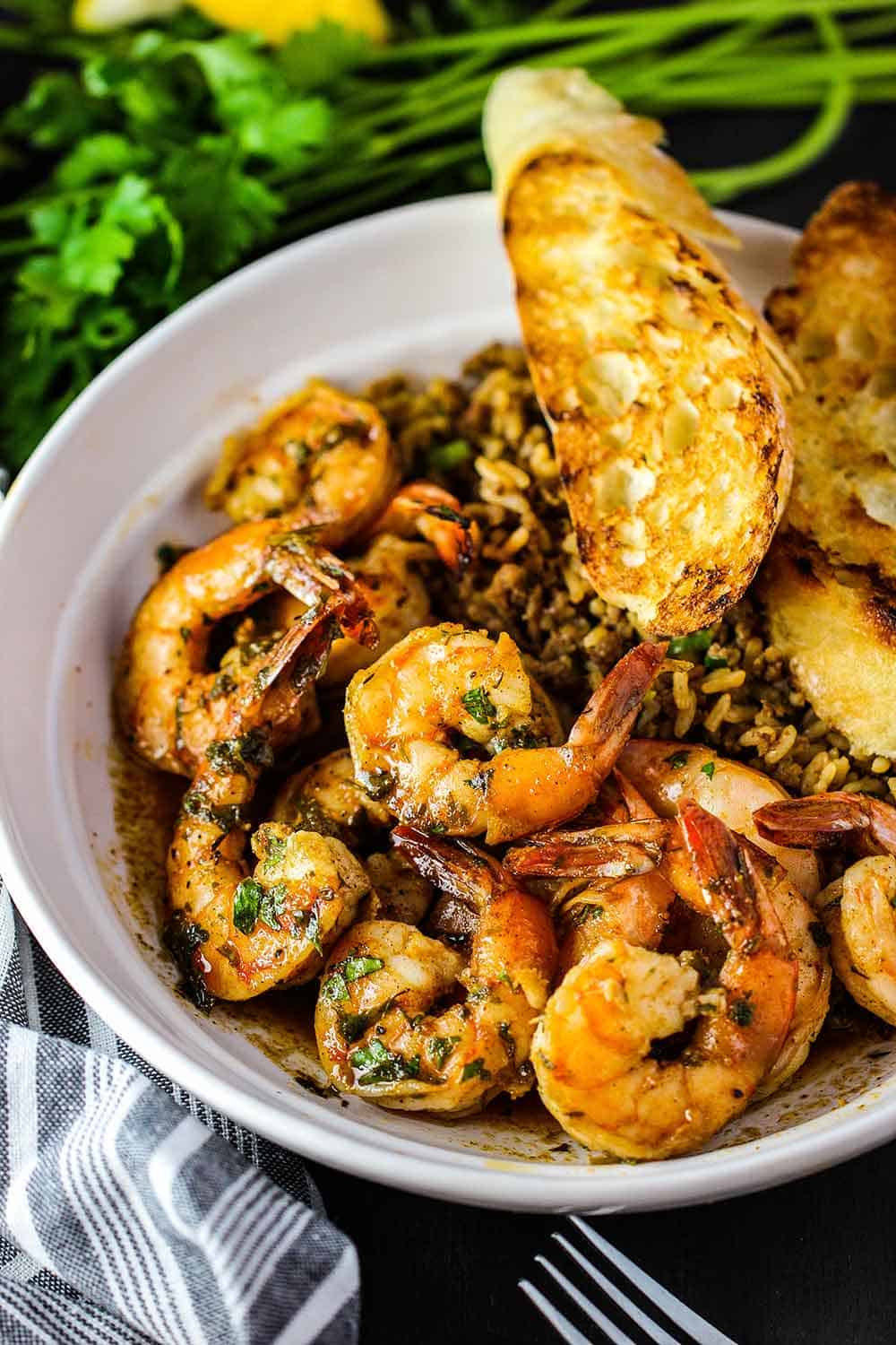 A white bowl containing Cajun bake shrimp, dirty rice and grilled bread. 