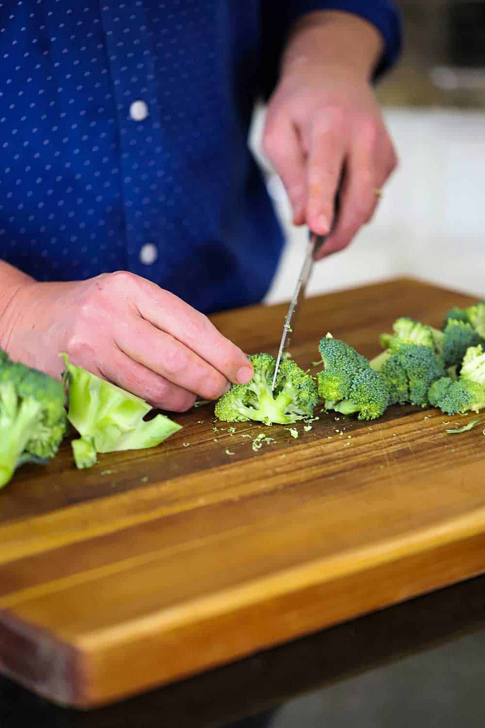 A person using a knife to cut fresh broccoli into florets on a wooden cutting board. 