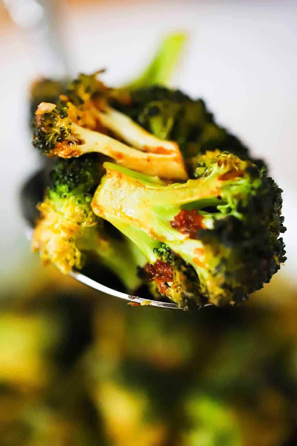 A large silver spoon holding up a helping of roasted broccoli with red pepper flakes on it. 