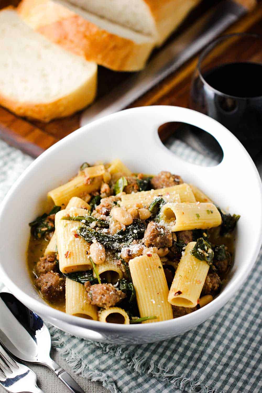 A white bowl of Country Italian Pasta next to sliced bread and a glass of red wine.