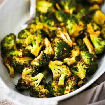 An oval white serving dish filled with roasted broccoli with a kick.