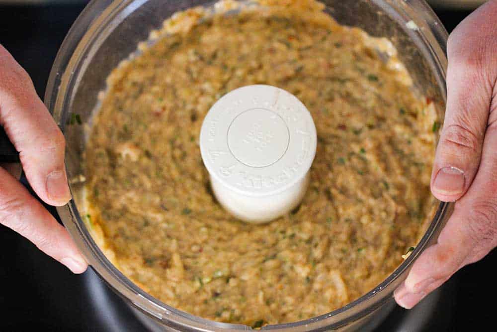 Two hands holding onto a large food processor filled with pureed ingredients for fried shrimp balls. 