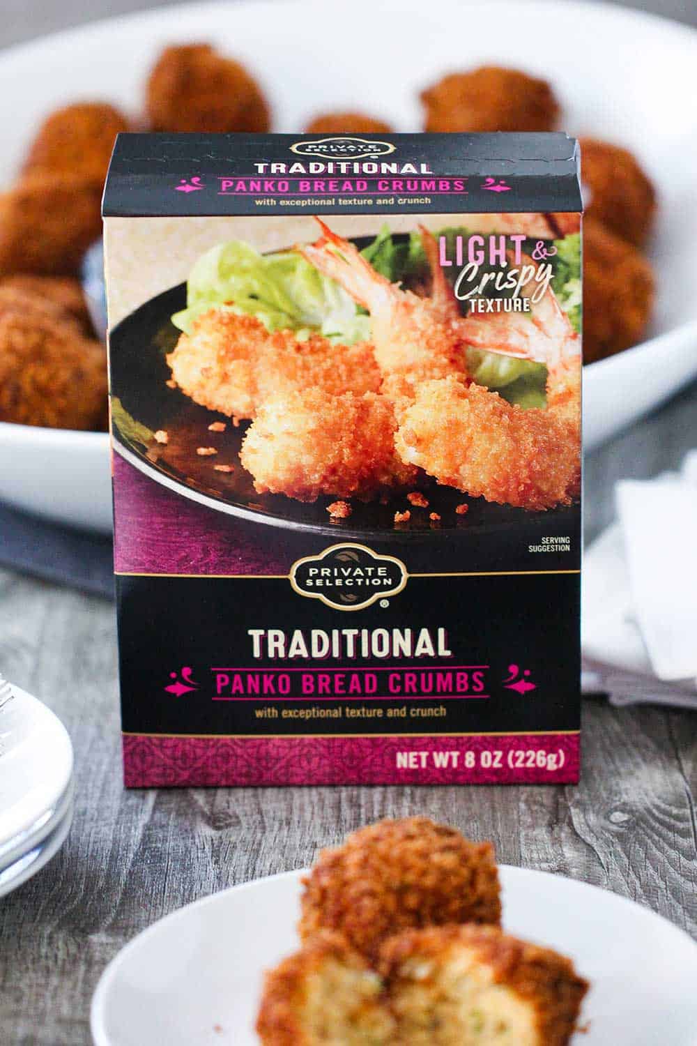 A box of Panko bread crumbs sitting behind a cocktail plate holding a split open fried shrimp ball. 