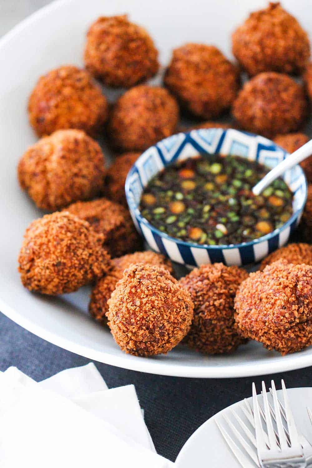 A large white bowl containing fried shrimp balls with a bowl of spicy dipping sauce in the middle. 