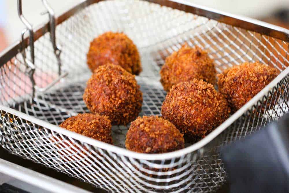 A deep-fryer basket holding 6 fried shrimp balls over the deep fryer. 