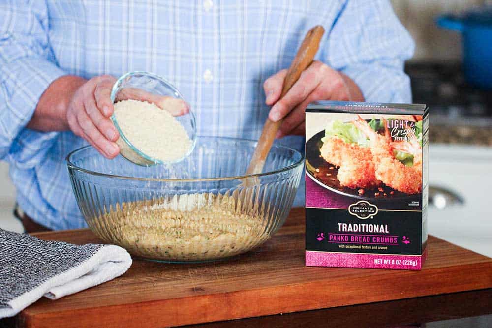 A person mixing Panko bread crumbs into a large glass bowl full of shrimp ball batter next to a box of Panko bread crumbs. 