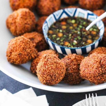 Fried shrimp balls on a platter surround a bowl of spicy dipping sauce.