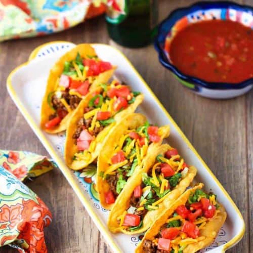 A plate of Authentic TexMex Tacos next to a patterned napking and a bowl of salsa