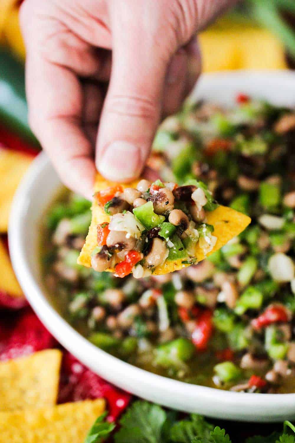 A hand holding a chip loaded with Texas Caviar over a bowl of the dip. 