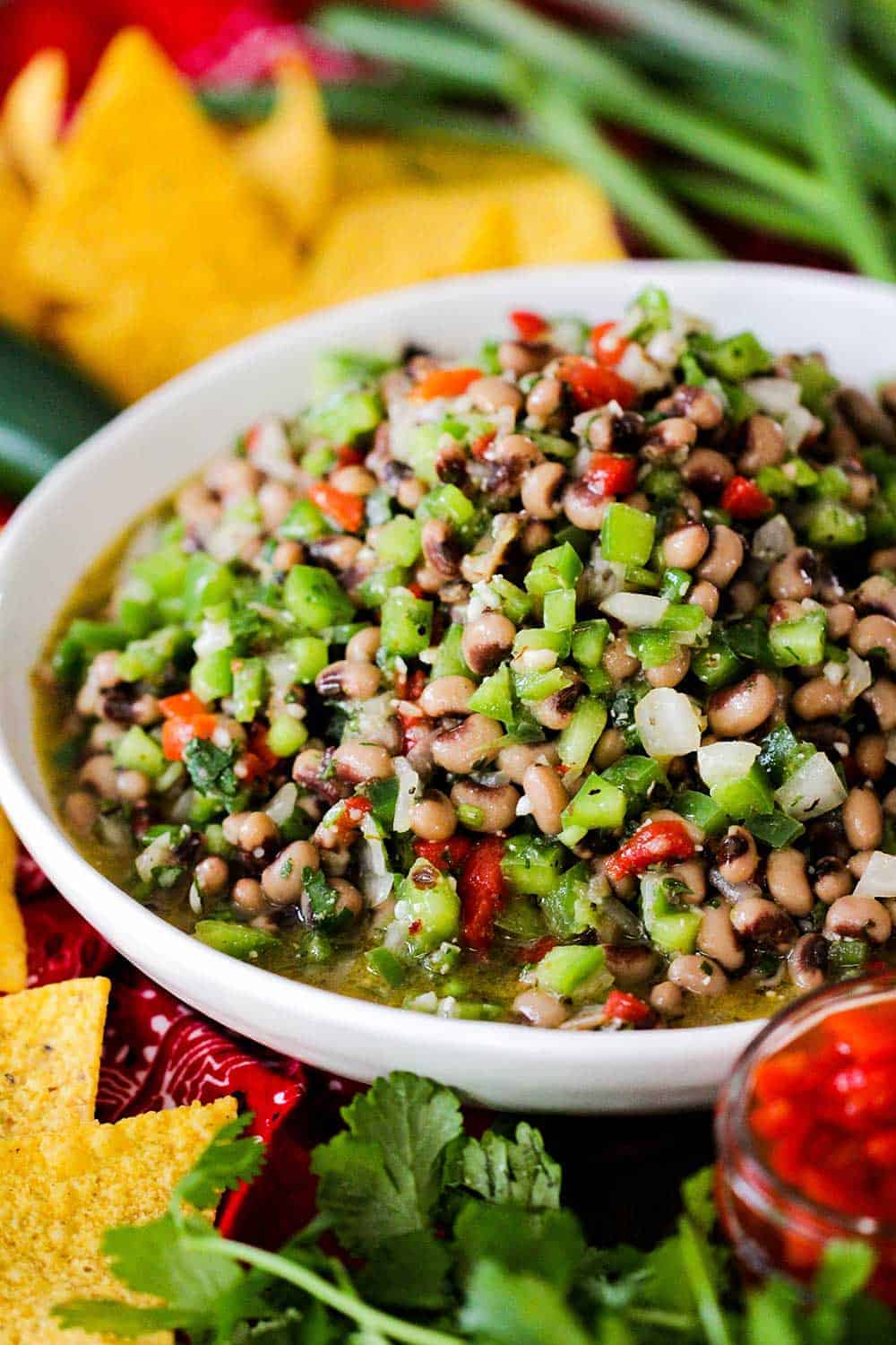 A large white bowl filled with Texas caviar surrounded by tortilla chips and scallions. 