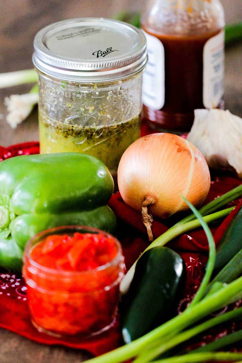 A cutting board topped with pimentos, green pepper, onion and a jar of Italian dressing. 