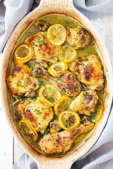 A large oval baking dish filled with lemon roast chicken pieces and lemon slices.