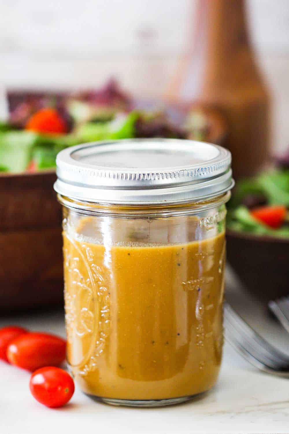 A Mason jar filled with homemade balsamic vinaigrette next to a wooden salad bowl filled with salad. 