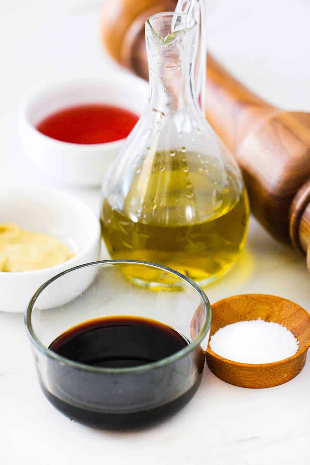 Various containers of vinegar, oil, mustard, and a pepper grinder on a white board. 