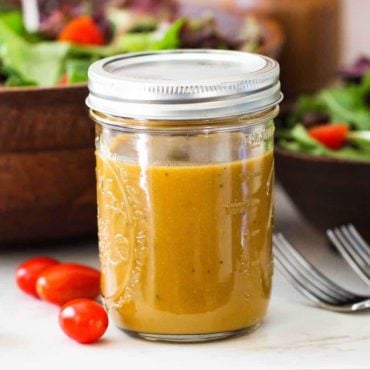 A Mason jar filled with homemade balsamic vinaigrette next to a wooden salad bowl filled with salad.