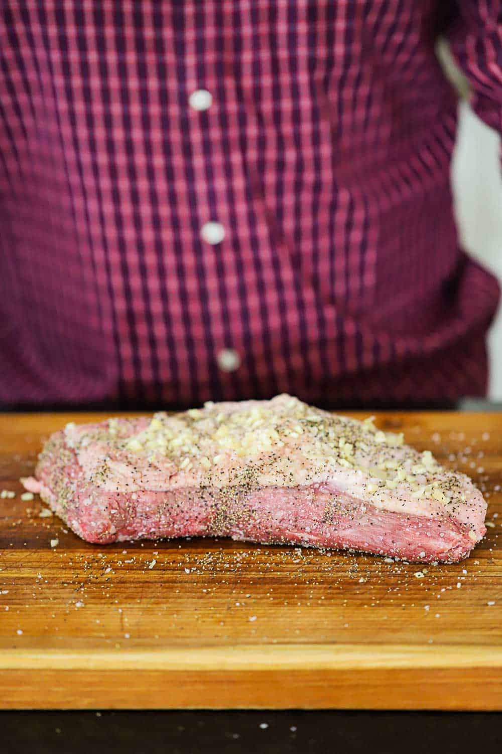 An uncooked brisket on a cutting board that has been seasoned with salt, pepper, and minced garlic. 