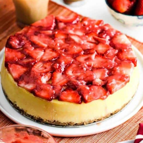 New York Style Cheese Cake with strawberries on top sitting next to a cup of coffee.