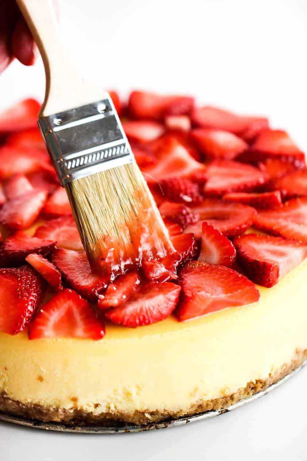 Brush applying a strawberry glaze on top of a New York cheese cake. 