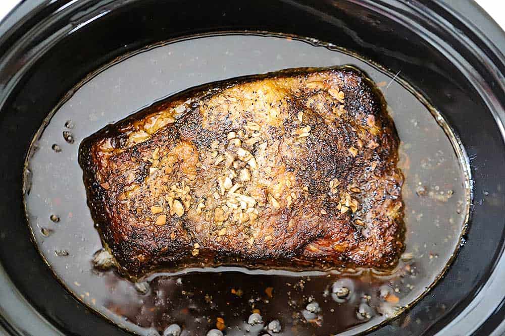 A fully cooked brisket in a slow cooker surround by dark juices. 