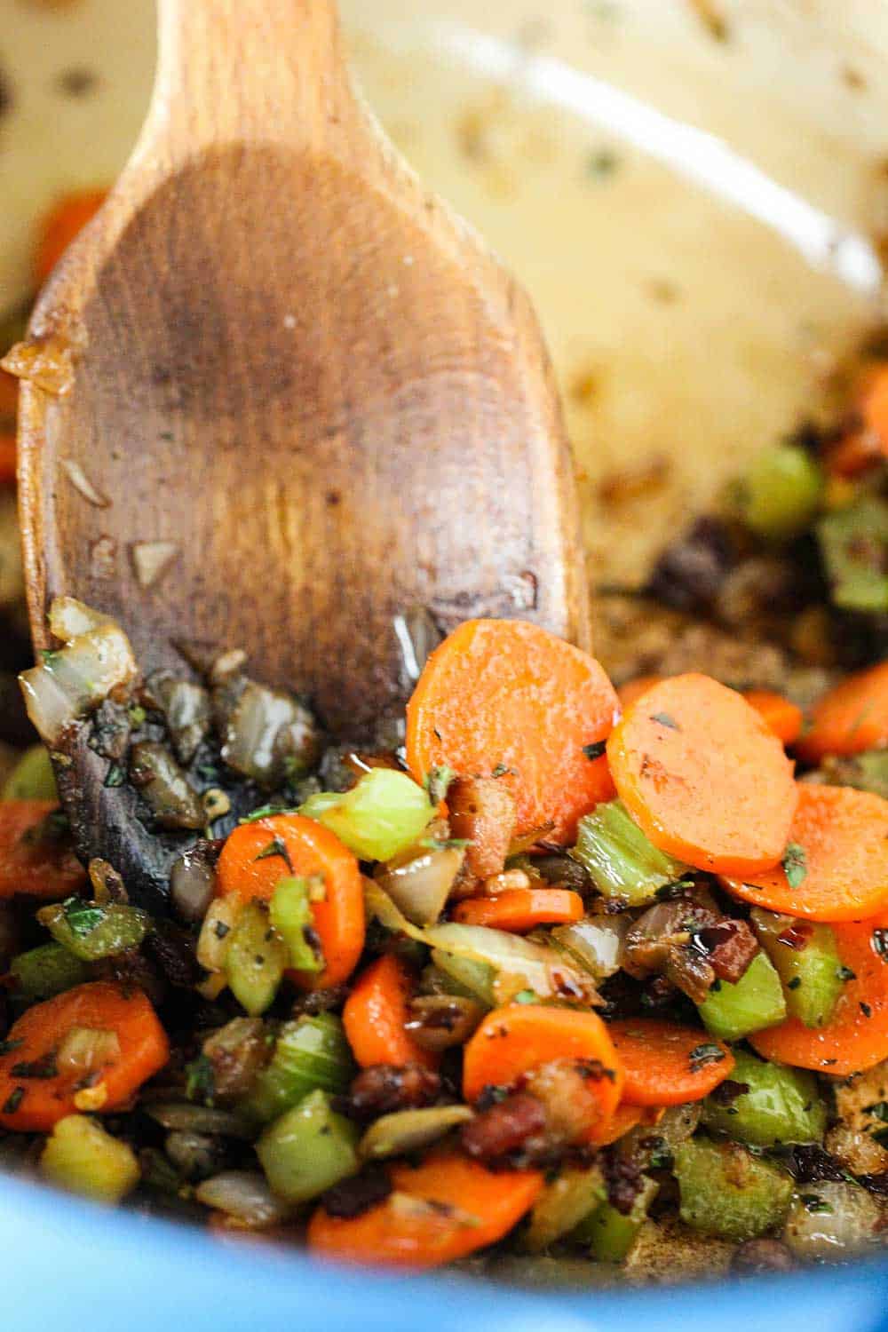 Sautéed carrots and onions in a Dutch oven with a wooden spoon in it. 