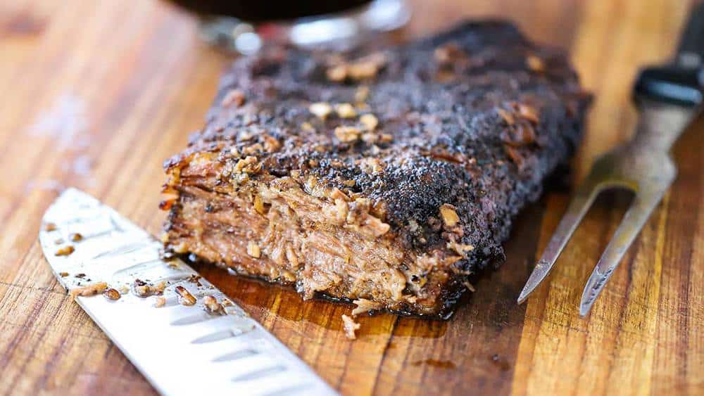 A slow cooker brisket sitting on a cutting board next to a large knife and an end slice missing. 