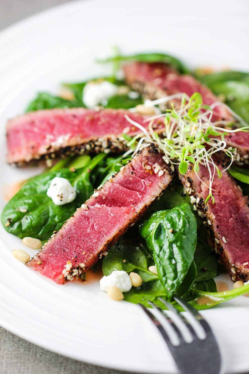 Slices of seared tuna steaks on top of a baby spinach salad. 