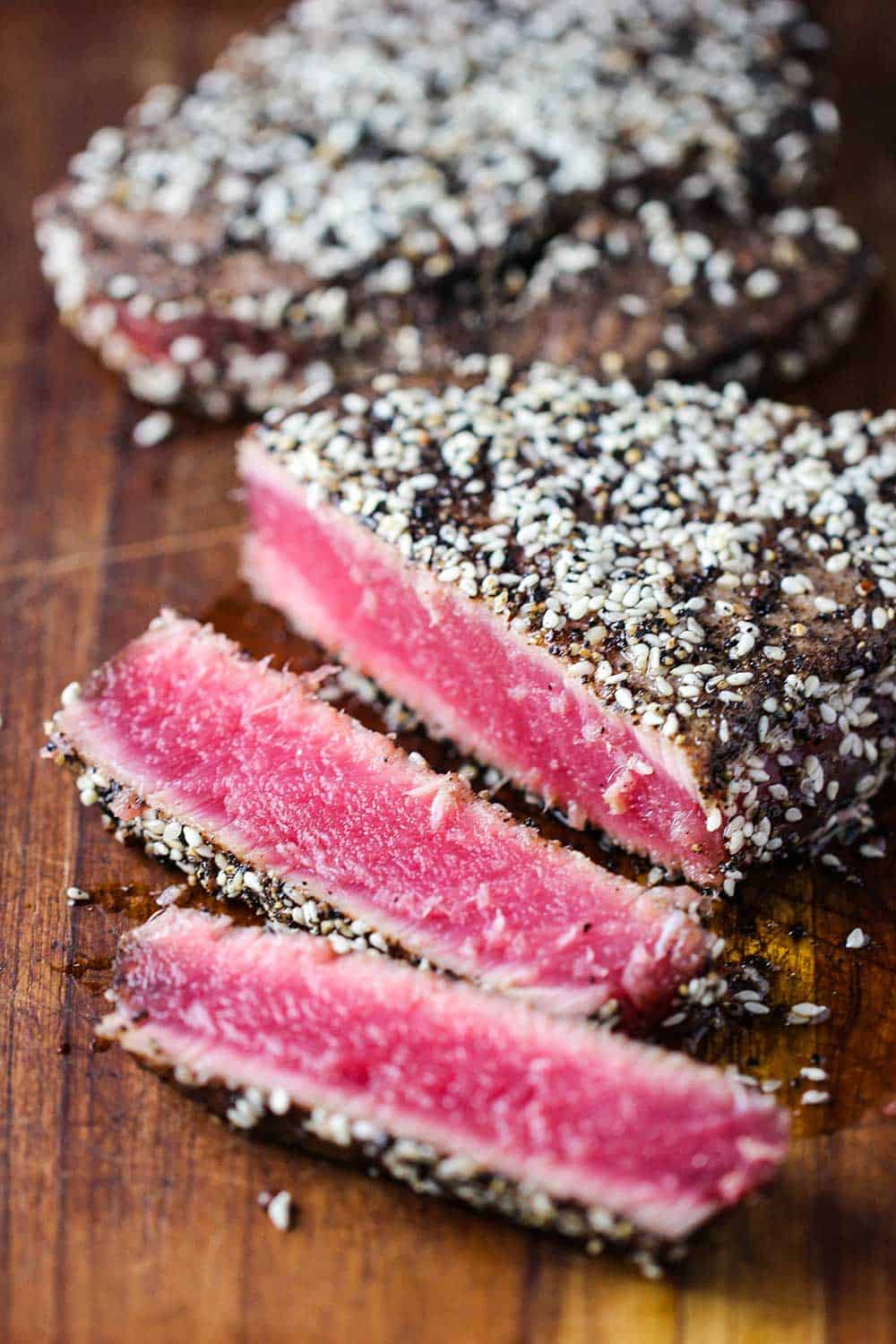 Seared peppercorn tuna steaks the have been sliced on a cutting board with bright pink center. 