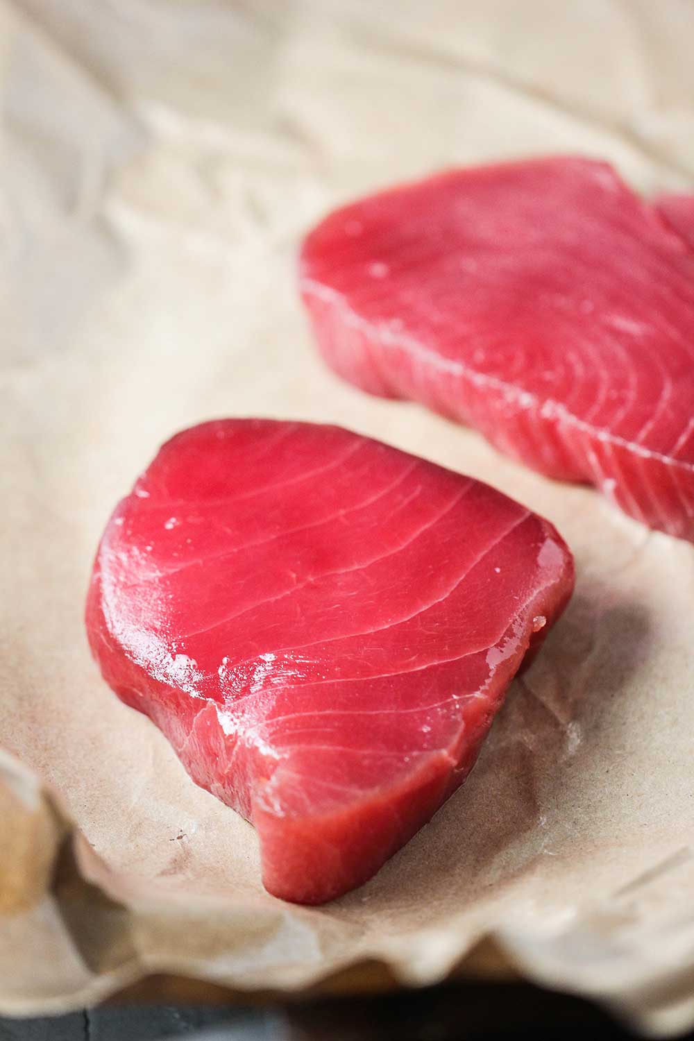 Two vibrant raw tuna steaks on butcher's paper. 