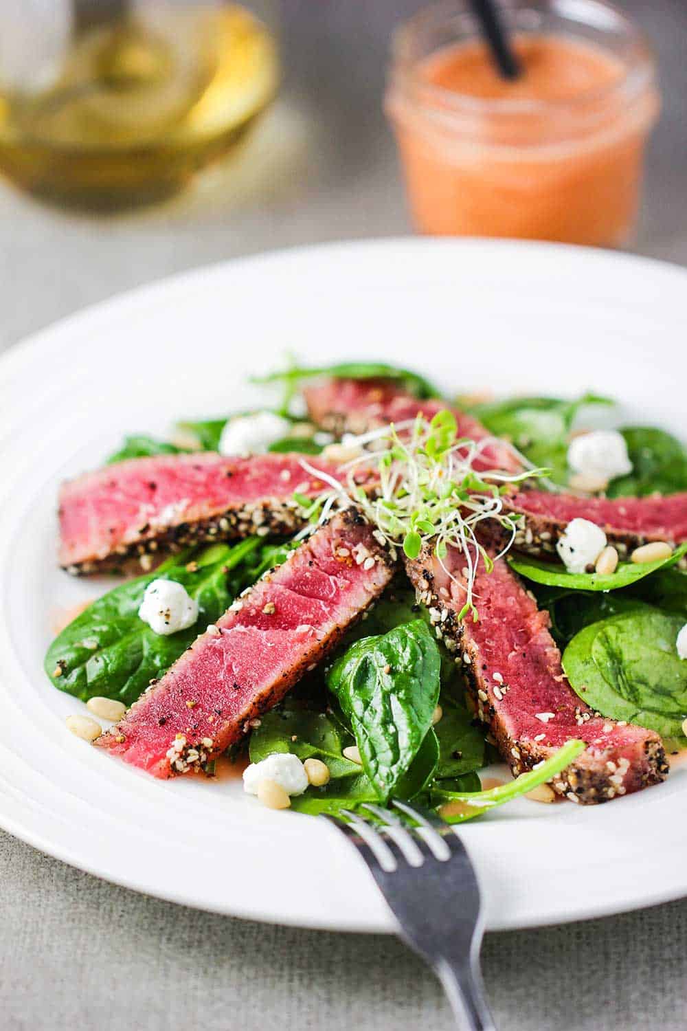 Slices of seared tuna steaks on top of a baby spinach salad. 
