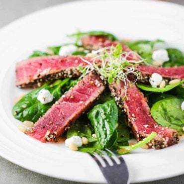 Slices of seared tuna steaks on top of a baby spinach salad.