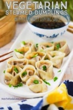 An oval white serving platter filled with vegetarian steamed dumplings sprinkled with chopped parsley.