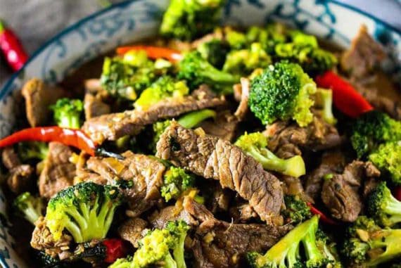 A bowl full of beef and broccoli stir-fry with chop sticks.
