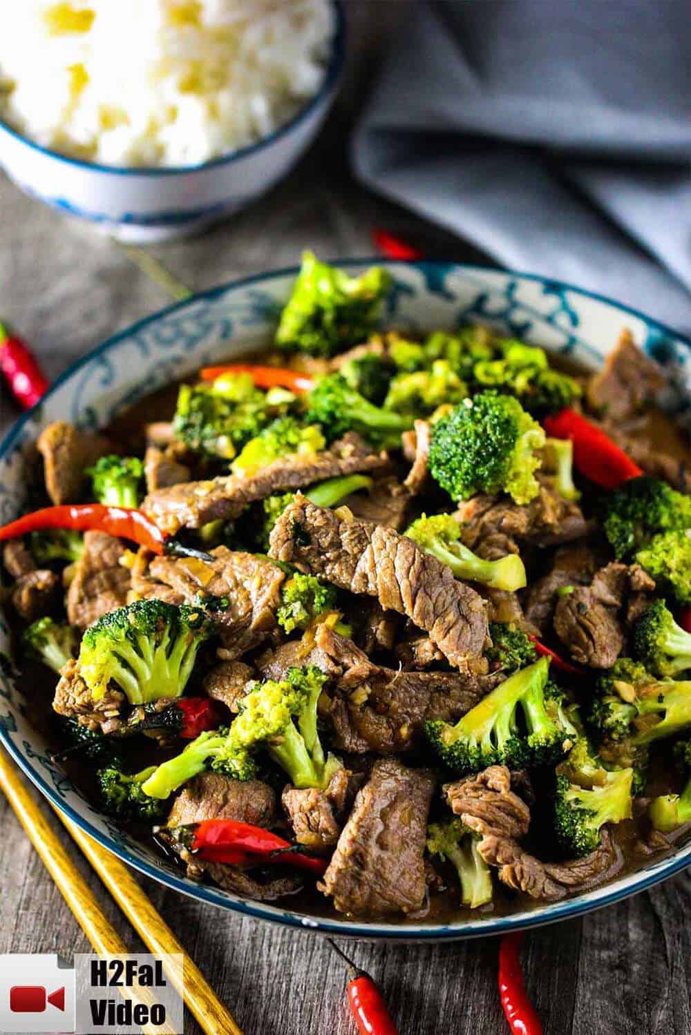 A bowl full of beef and broccoli stir-fry with chop sticks.