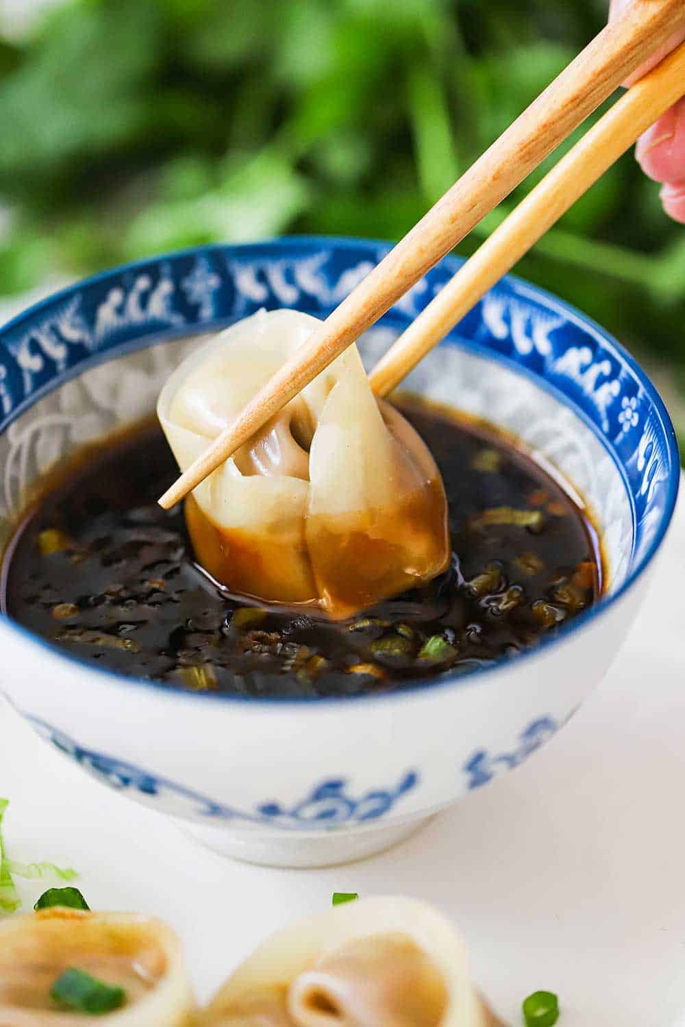 A person using two chopsticks to dunk a steamed dumpling into a small Asian bowl filled with hot and sweet dipping sauce.