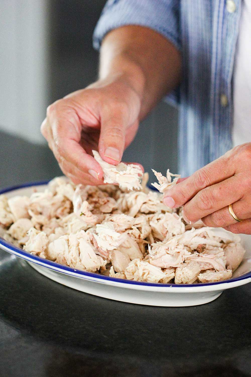 Two hands shredding cooked chicken for homemade chicken and dumplings. 