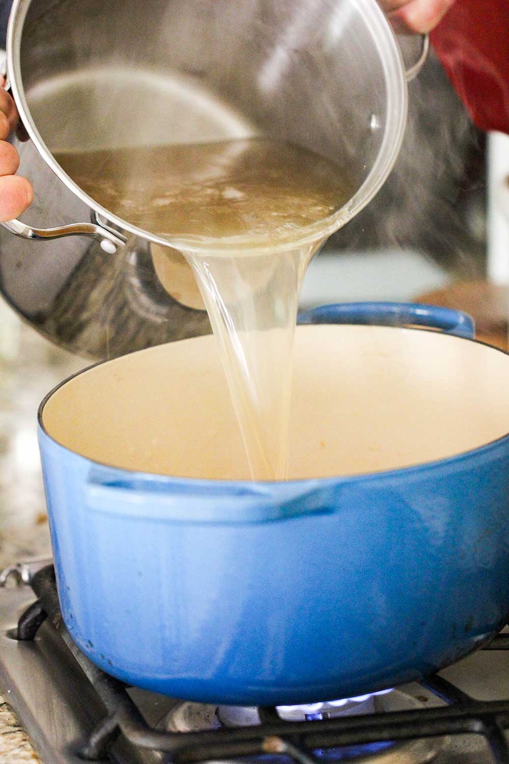 A stock pot of chicken broth pouring into a large Dutch oven. 