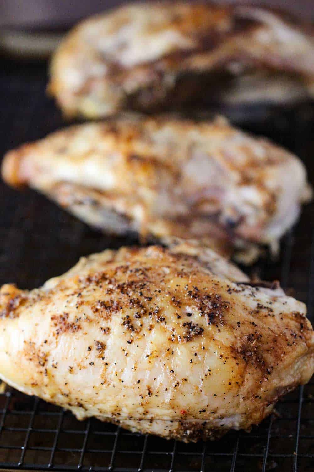 Three roasted chicken breasts on a baking rack on top of baking sheet. 