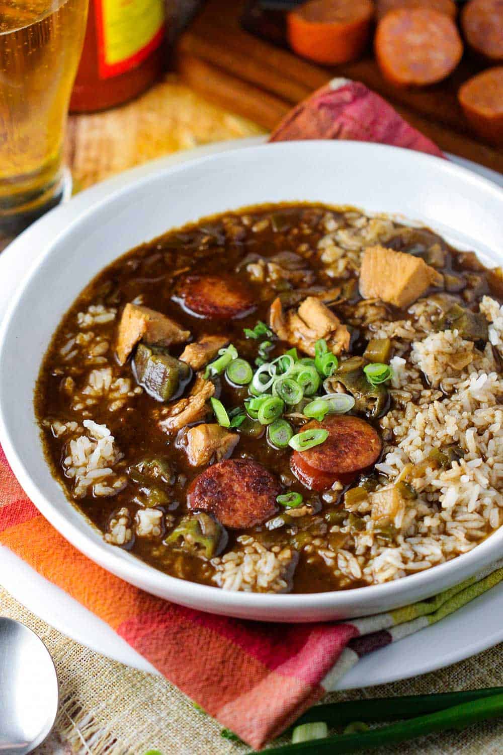 A white bowl chicken and sausage gumbo on top of patterned napkin with a spoon next to it.